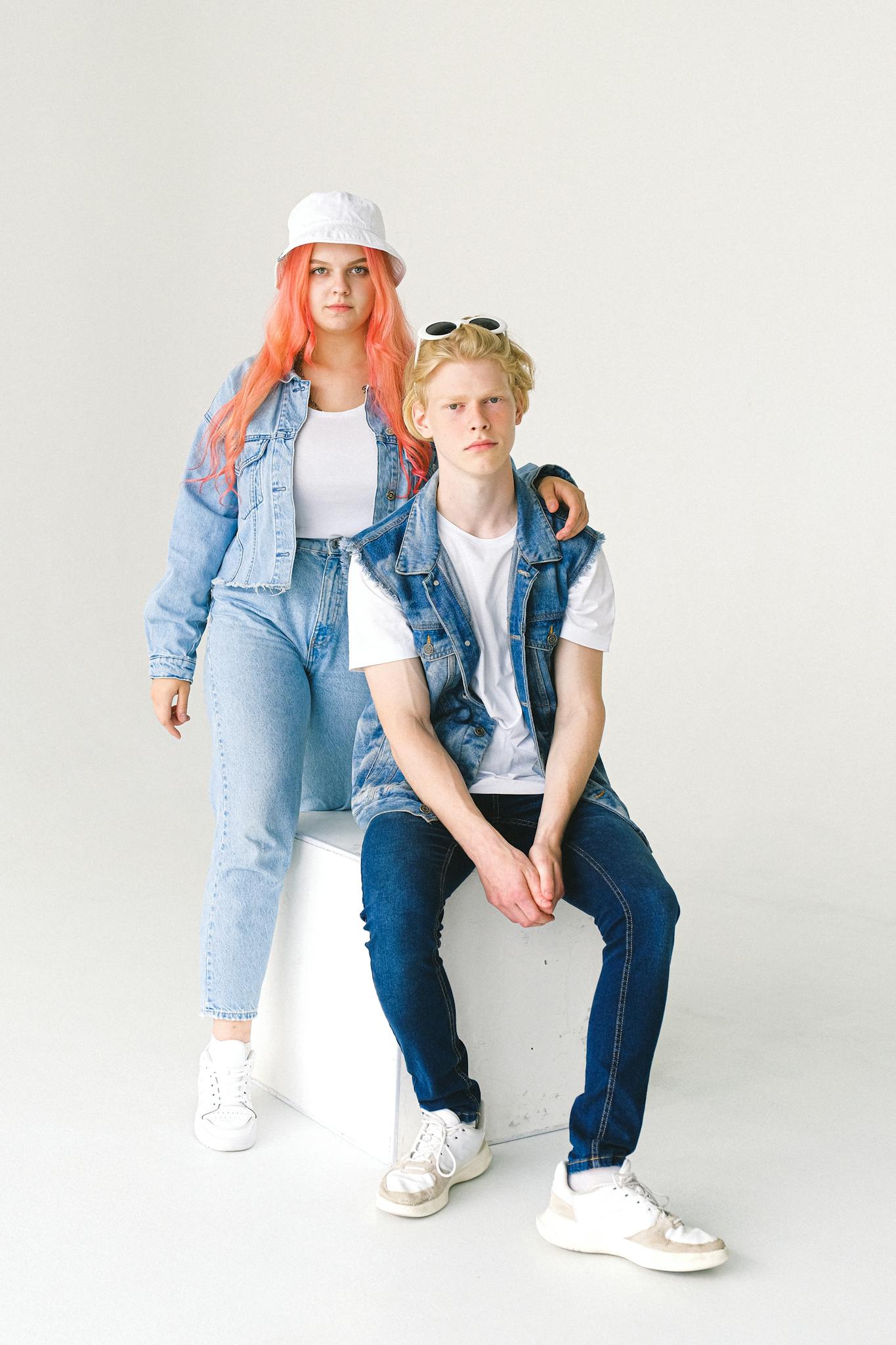 Full body of unemotional teens wearing trendy denim outfits and sneakers in studio